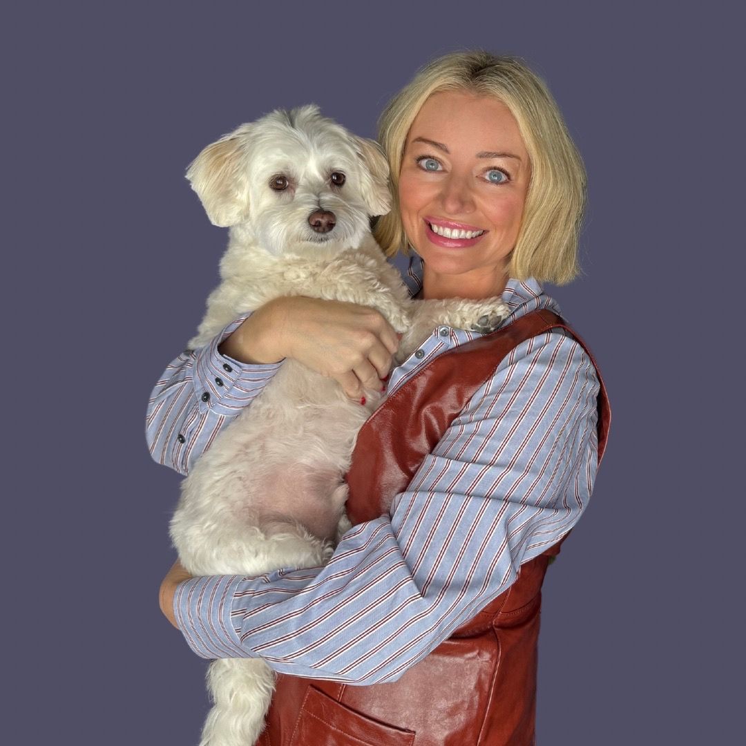 Smiling woman holding a fluffy white dog against a solid purple background.