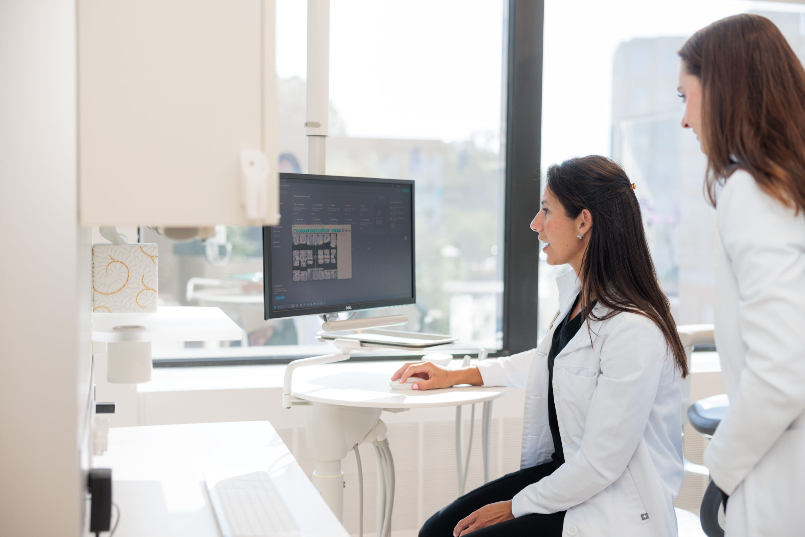 Two medical professionals reviewing dental scans on a computer screen.
