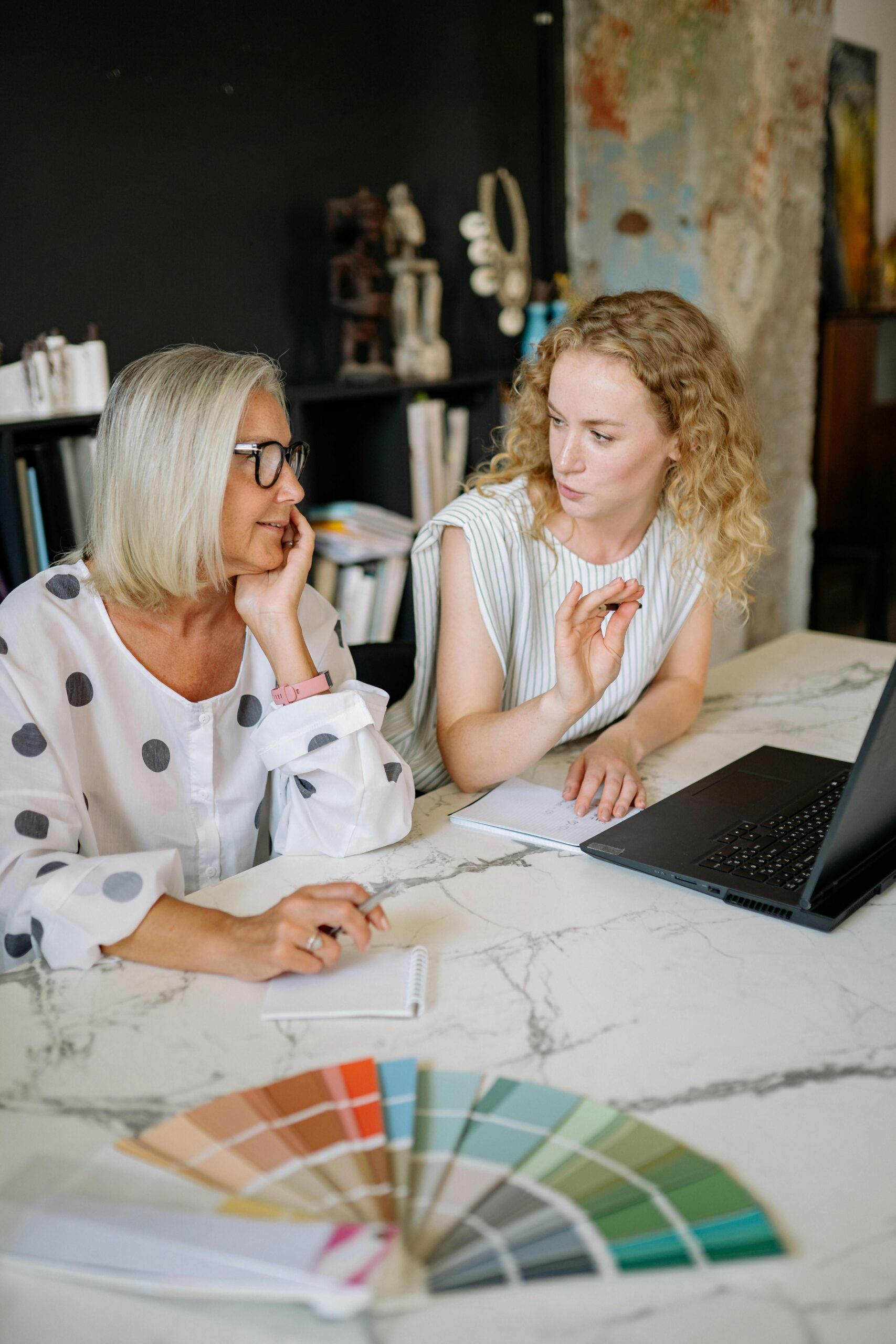 Two women discussing color swatches and design ideas with a laptop at a creative workspace.